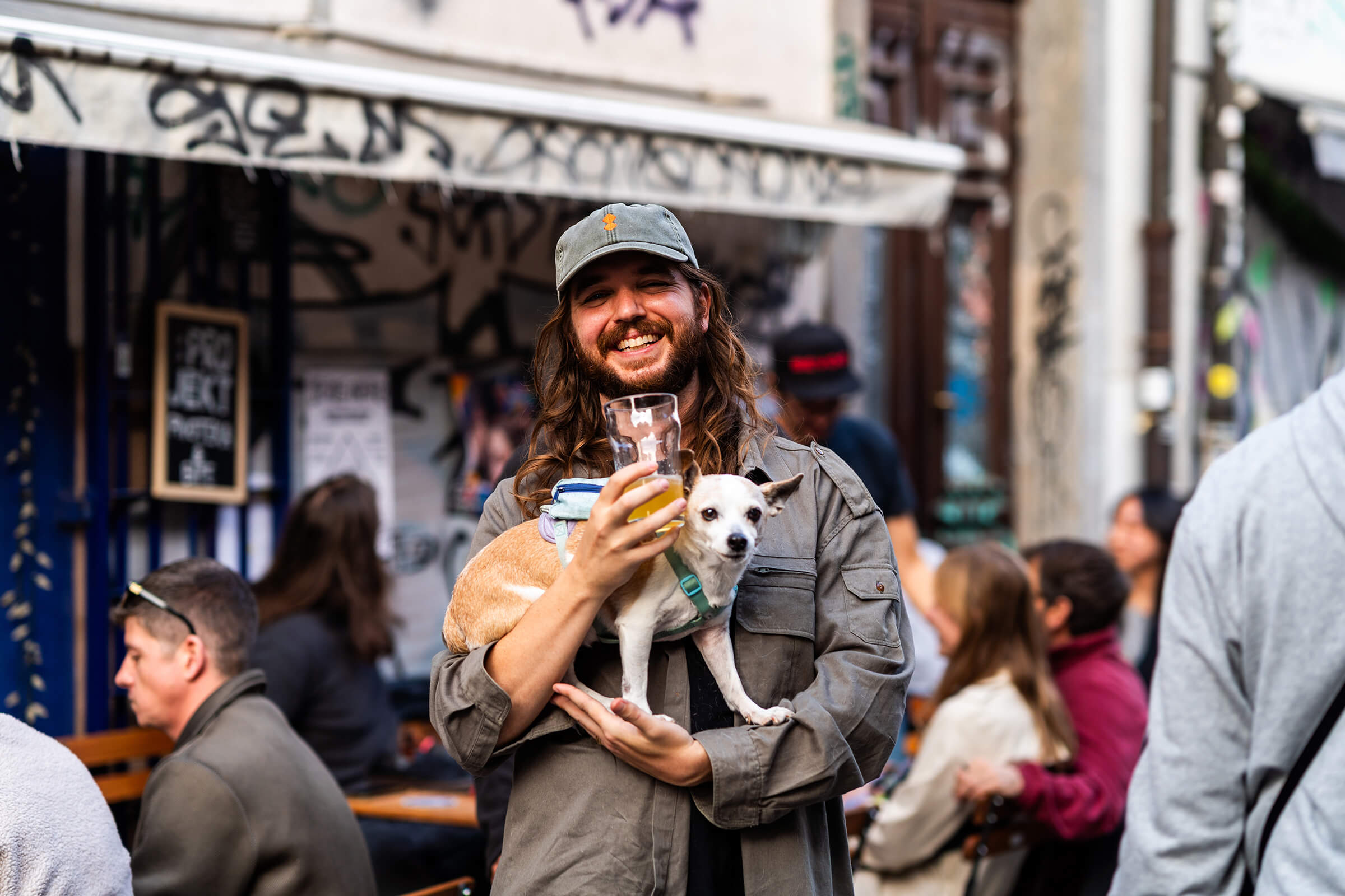 Smiling guest holding a beer and a small dog outside :Projekt at the Folk Hero grand opening