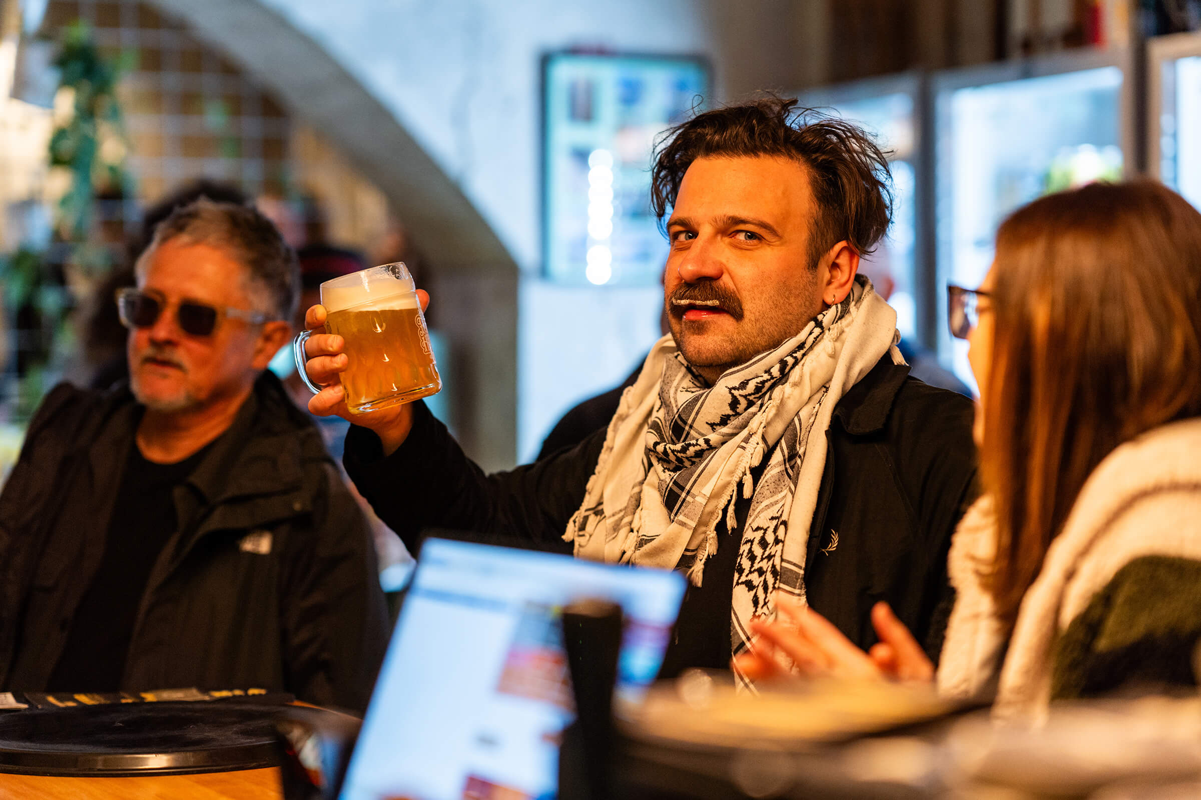 Guest in a scarf raising a beer at the bar during the Folk Hero grand opening